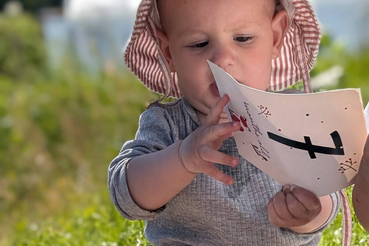 Beba sa šeširićem drži karticu sa slovom i pažljivo je gleda